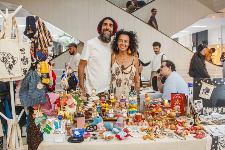 Expositores sorrindo atrás de uma mesa de artesanato (julho de 2026)